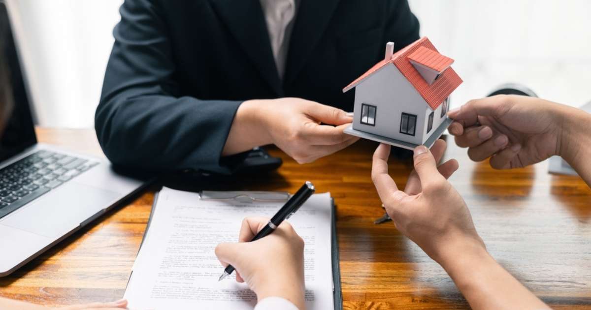 A couple stands together, each holding a miniature house model, representing their shared dream of homeownership.